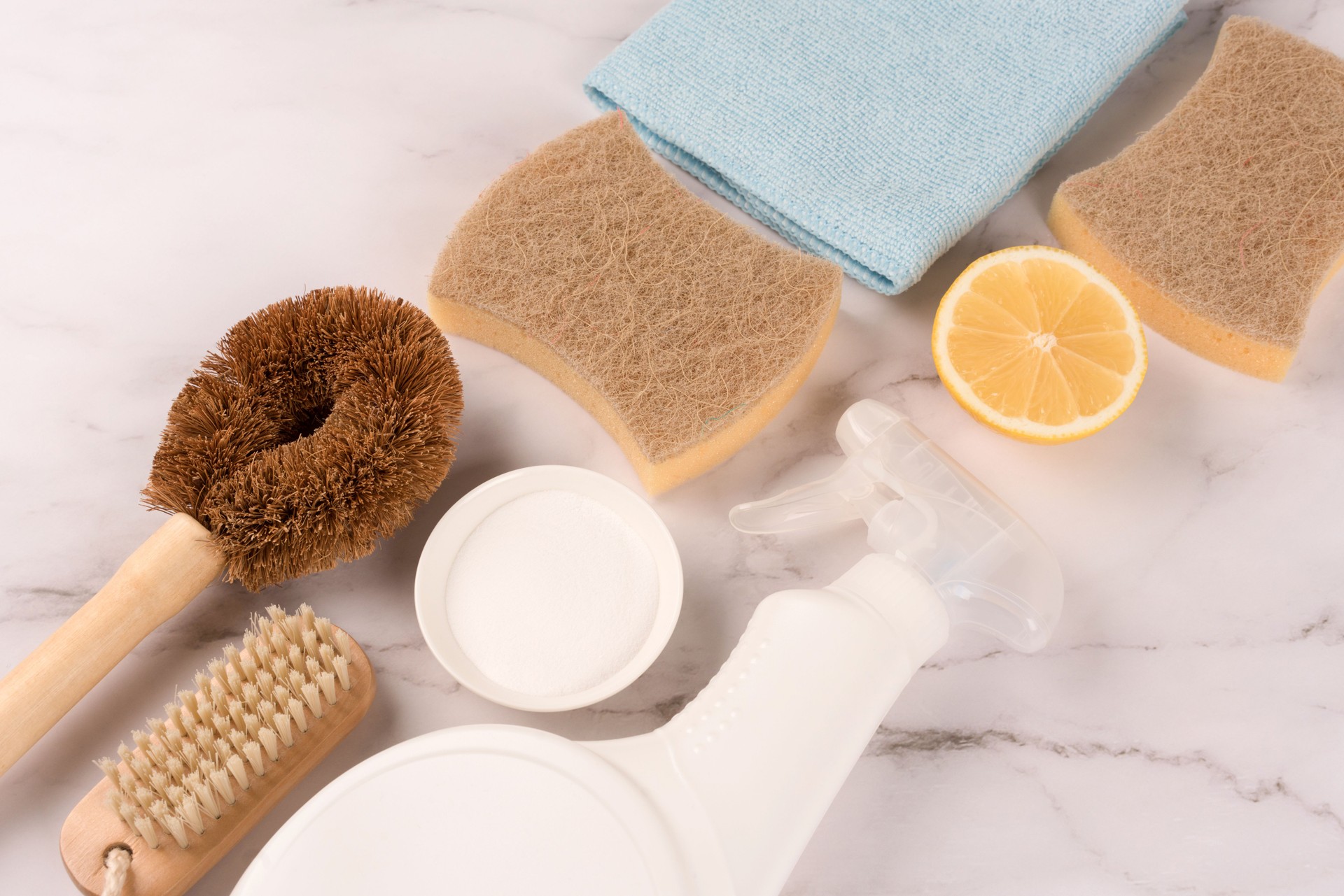 Natural household cleaners for green household - bamboo brush, organic dishcloth, lemon, baking soda, citric acid, spray bottle with cleaning liquid on marble background. Top view, mockup